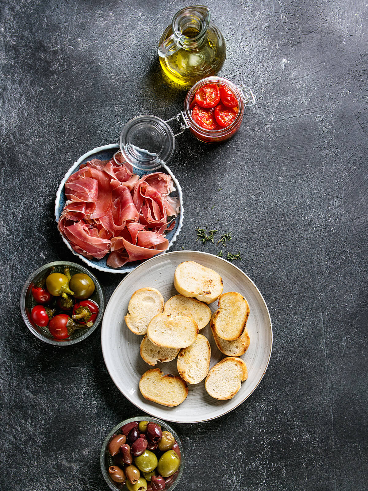 Tapas-Häppchen mit Ofentomaten, Serrano und Oliven auf gerösteten Baguette-Scheiben