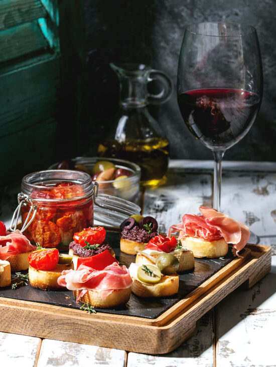 Tapas-Brett mit Serrano-Häppchen, Oliven und einem Glas eingelegter Tomaten bei Wein