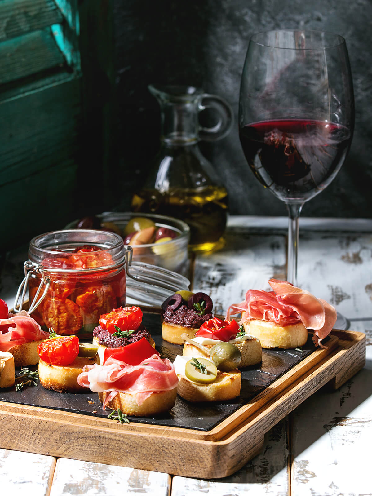 Tapas-Brett mit Serrano-Häppchen, Oliven und einem Glas eingelegter Tomaten bei Wein