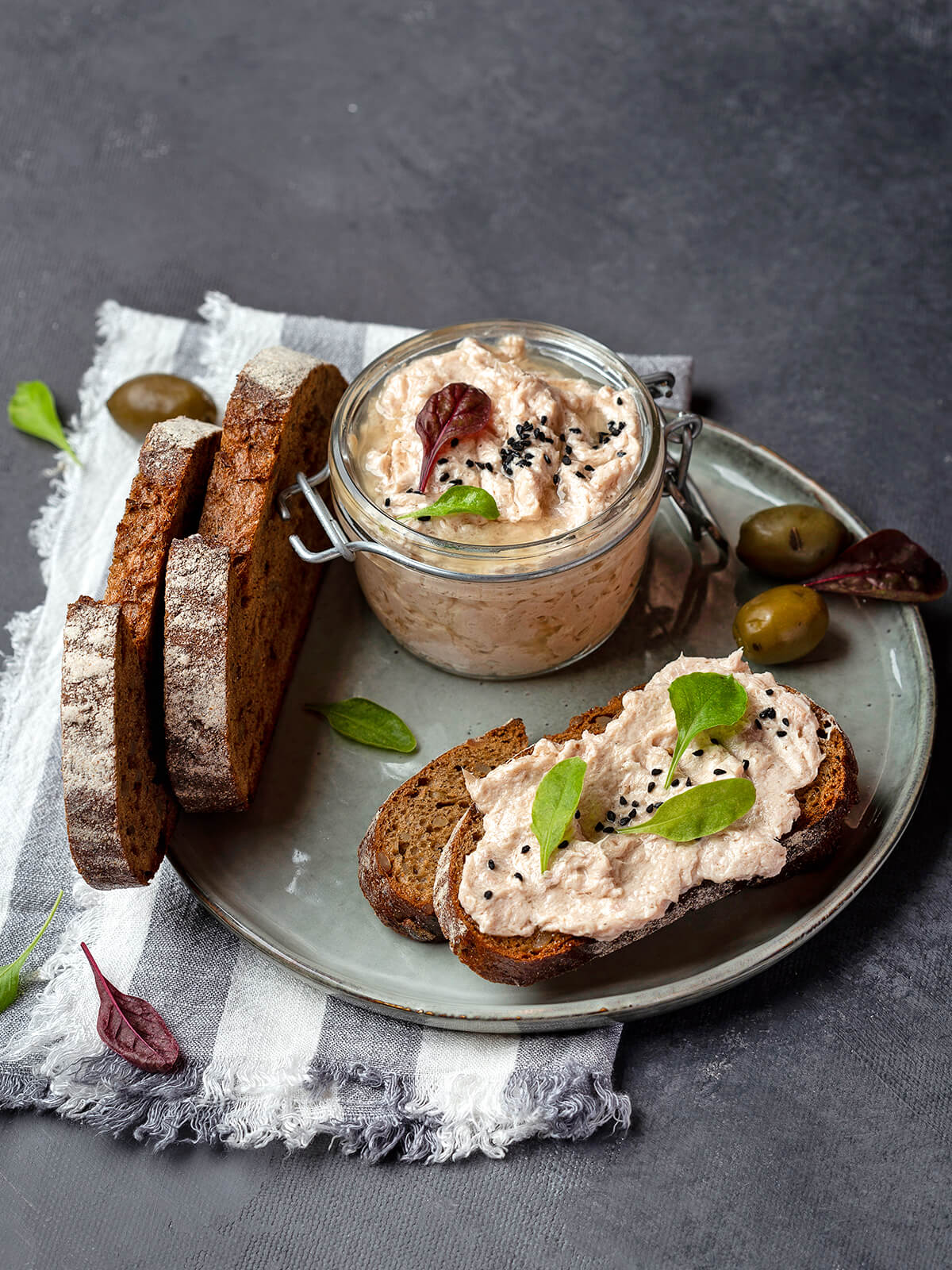 Thunfisch-Rillettes auf einer Scheibe dunklem Landbrot mit schwarzem Sesam und Blattspitzen