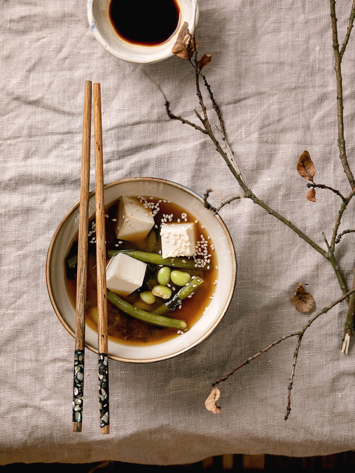 Schale Tofu-Miso-Suppe mit Tofuwürfeln, grünen Bohnen, Edamame und Sesam neben Stäbchen