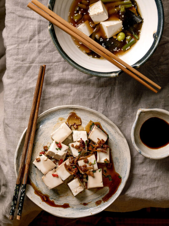 Schale Miso-Suppe neben einem Teller mit Seidentofu-Würfeln und Röstzwiebeln
