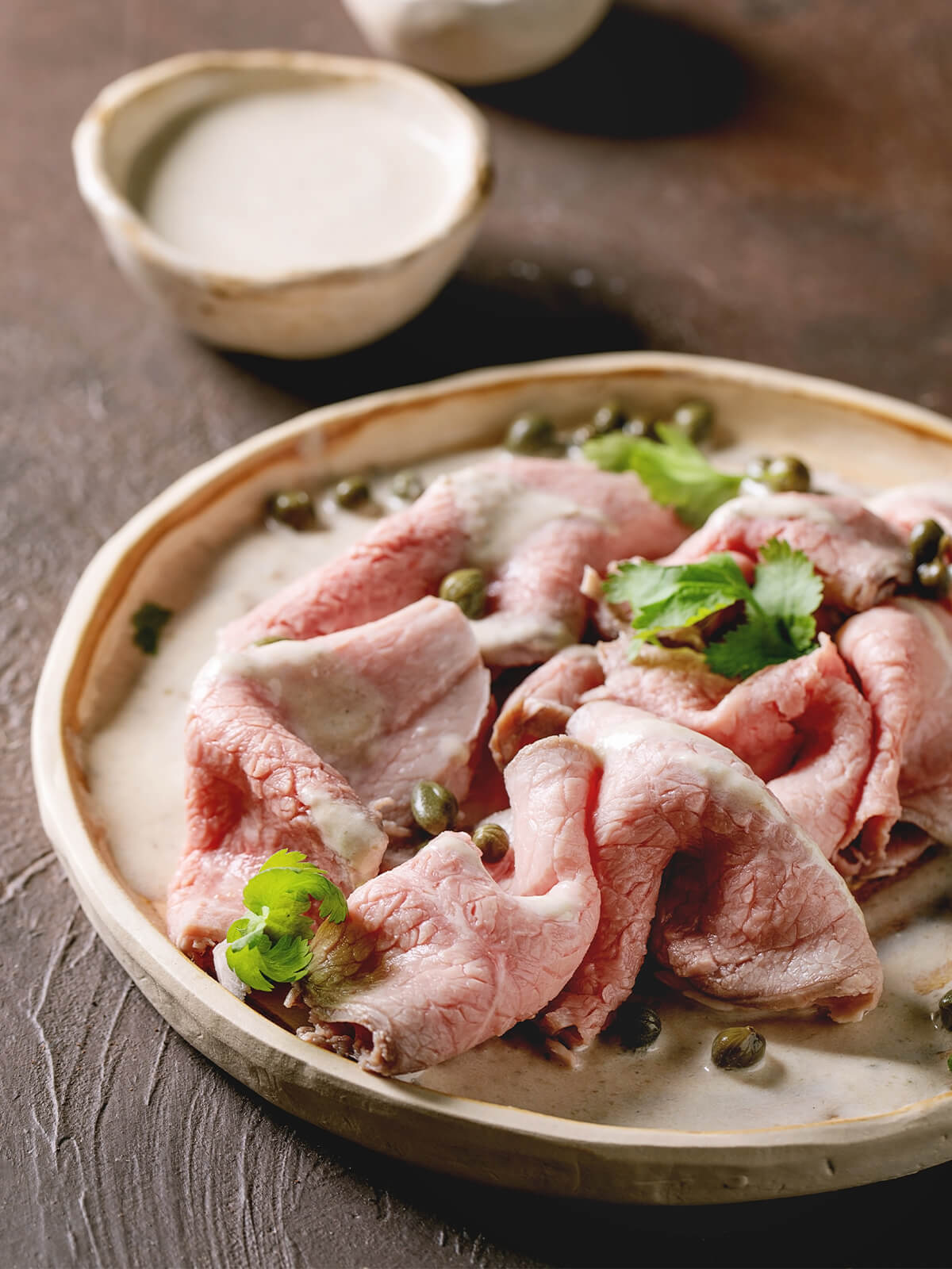 Vitello Tonnato auf heller Platte, dünne Kalbfleischscheiben unter cremiger Thunfisch-Soße mit Kapern