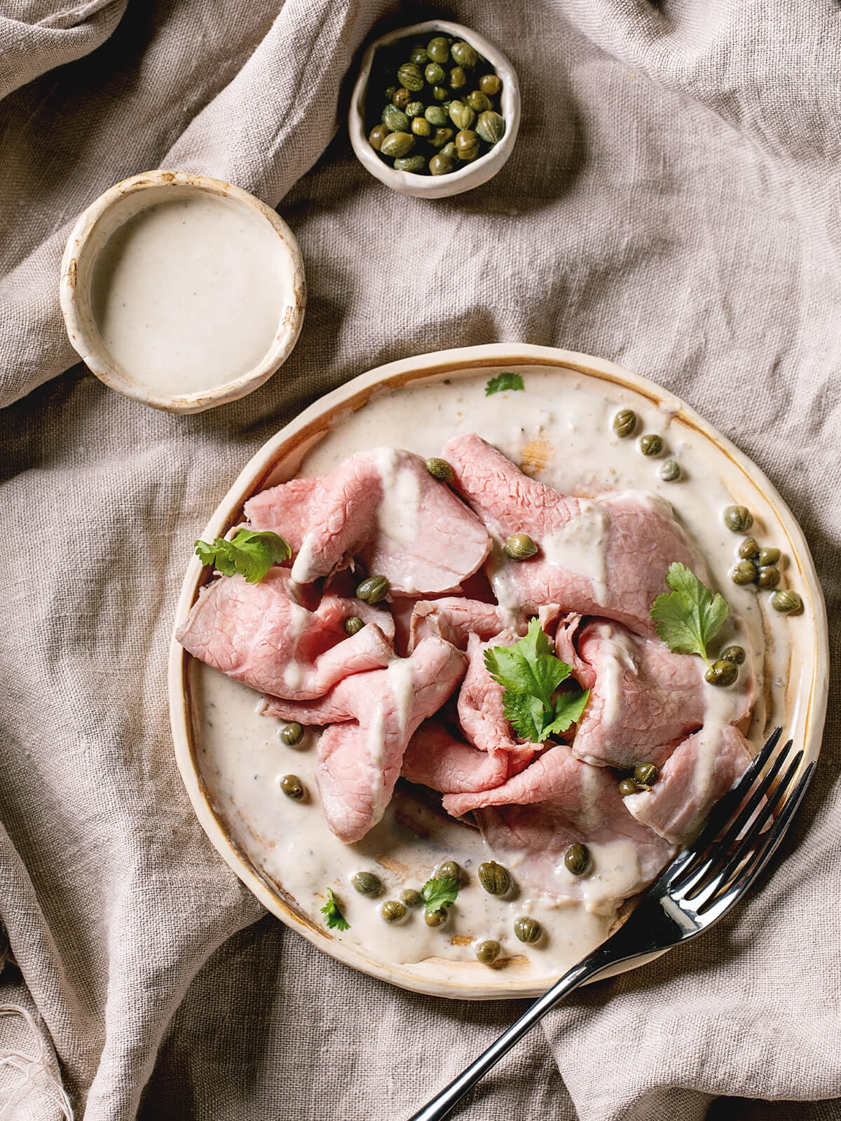Komponenten für Vitello Tonnato – Kalbfleischscheiben, Schälchen mit Thunfisch-Soße und Kapern