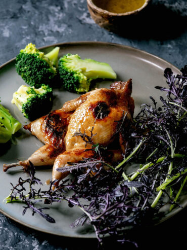 Asia-glasierte Wachtel auf weißem Teller mit Brokkoli und violetten Microgreens