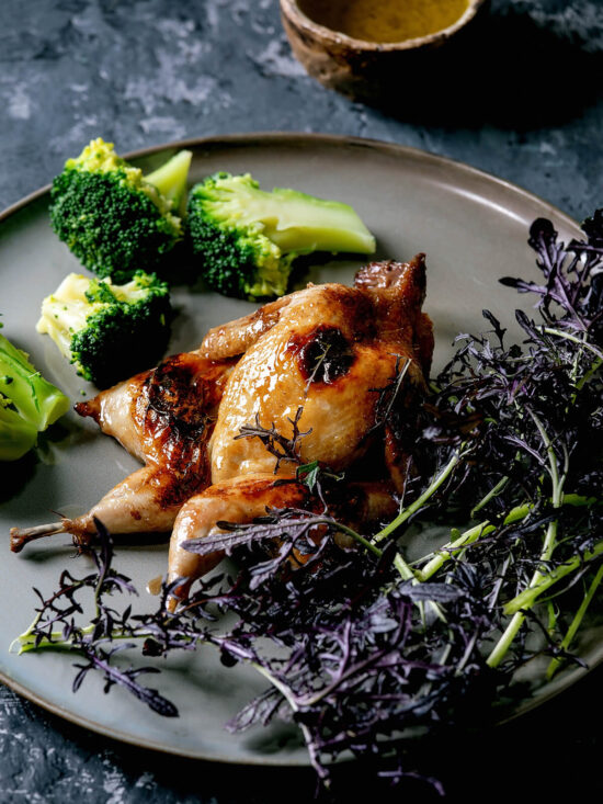 Asia-glasierte Wachtel auf weißem Teller mit Brokkoli und violetten Microgreens