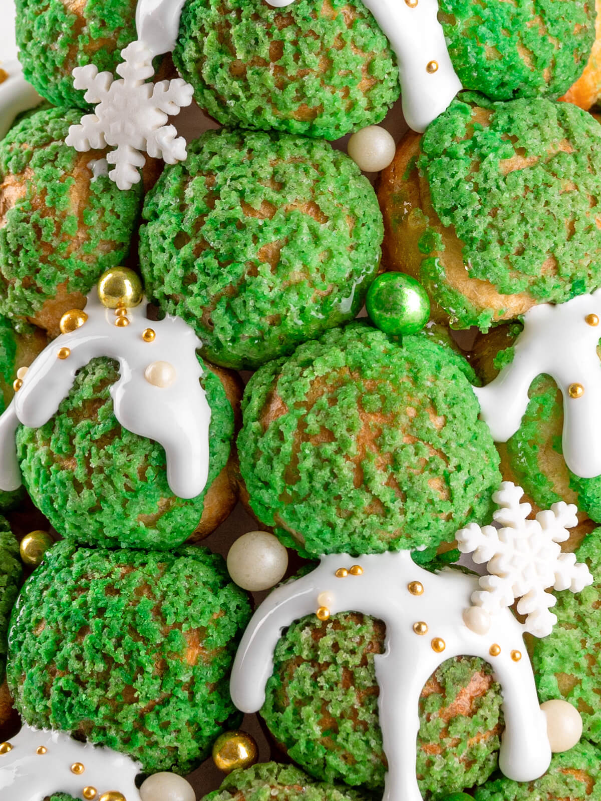 Nahaufnahme der grünen Craquelin-Windbeutel mit weißem Zuckerguss, goldenen Zuckerperlen und kleinen Zucker-Schneeflocken