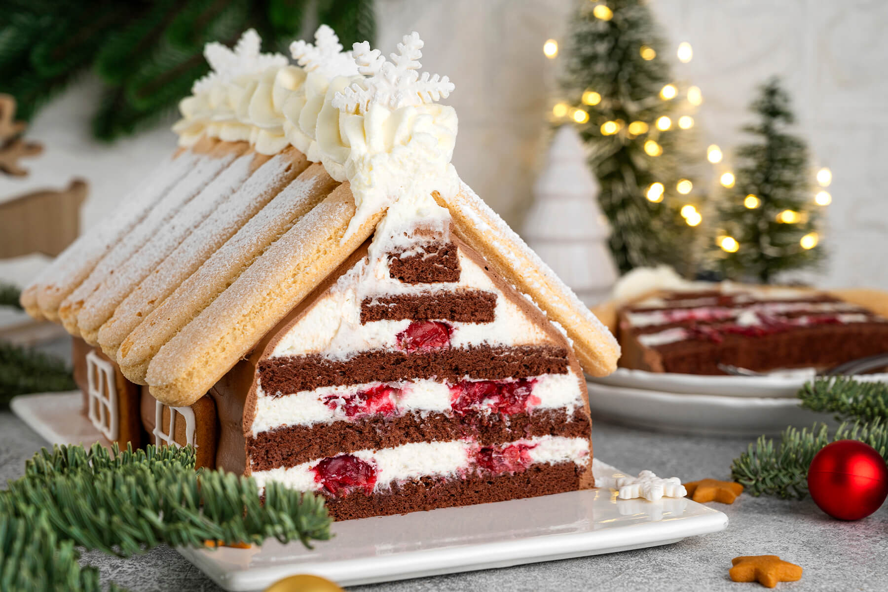 Angeschnittener Schoko-Hauskuchen mit Sahne-Kirsch-Schichten und Tannenzweigen