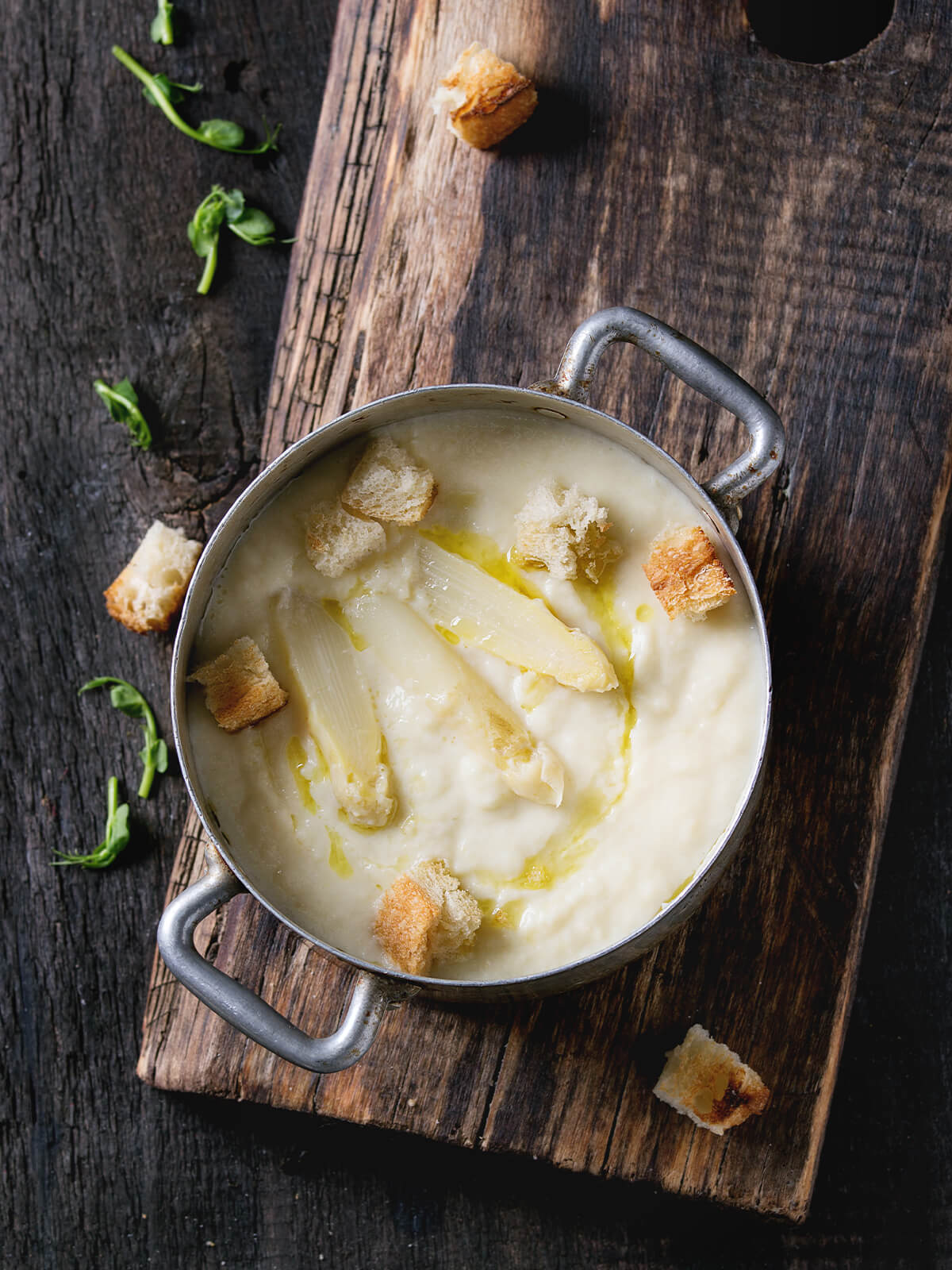 Weiße Spargel-Cremesuppe im kleinen Topf mit Croûtons, Olivenöl und Erbsensprossen