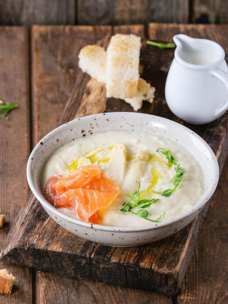 Weiße Spargel-Cremesuppe mit Sahne, Croûtons und frischen Kräutern in heller Schale