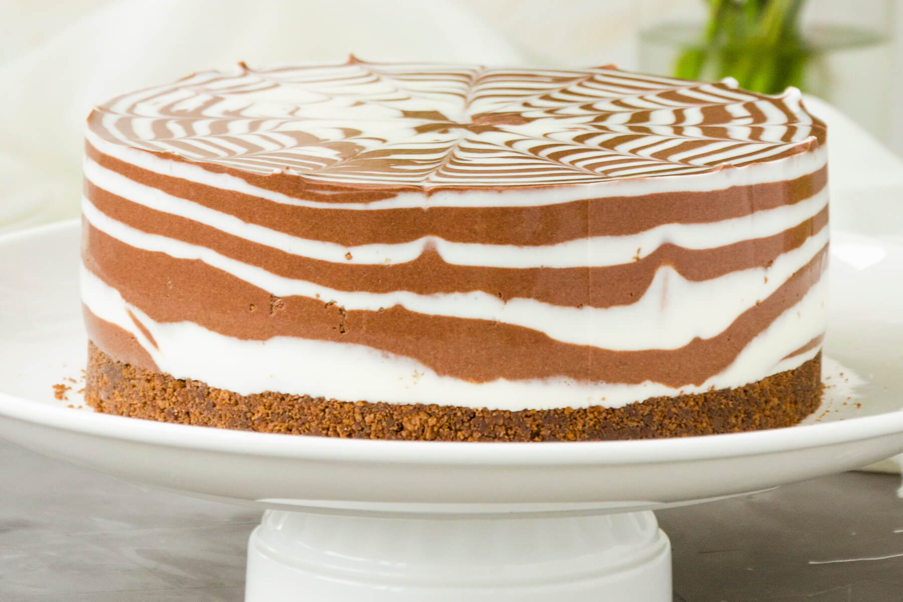 Ganzer Zebra-Marmor-Cheesecake auf weißer Tortenplatte mit gestreiftem Rand