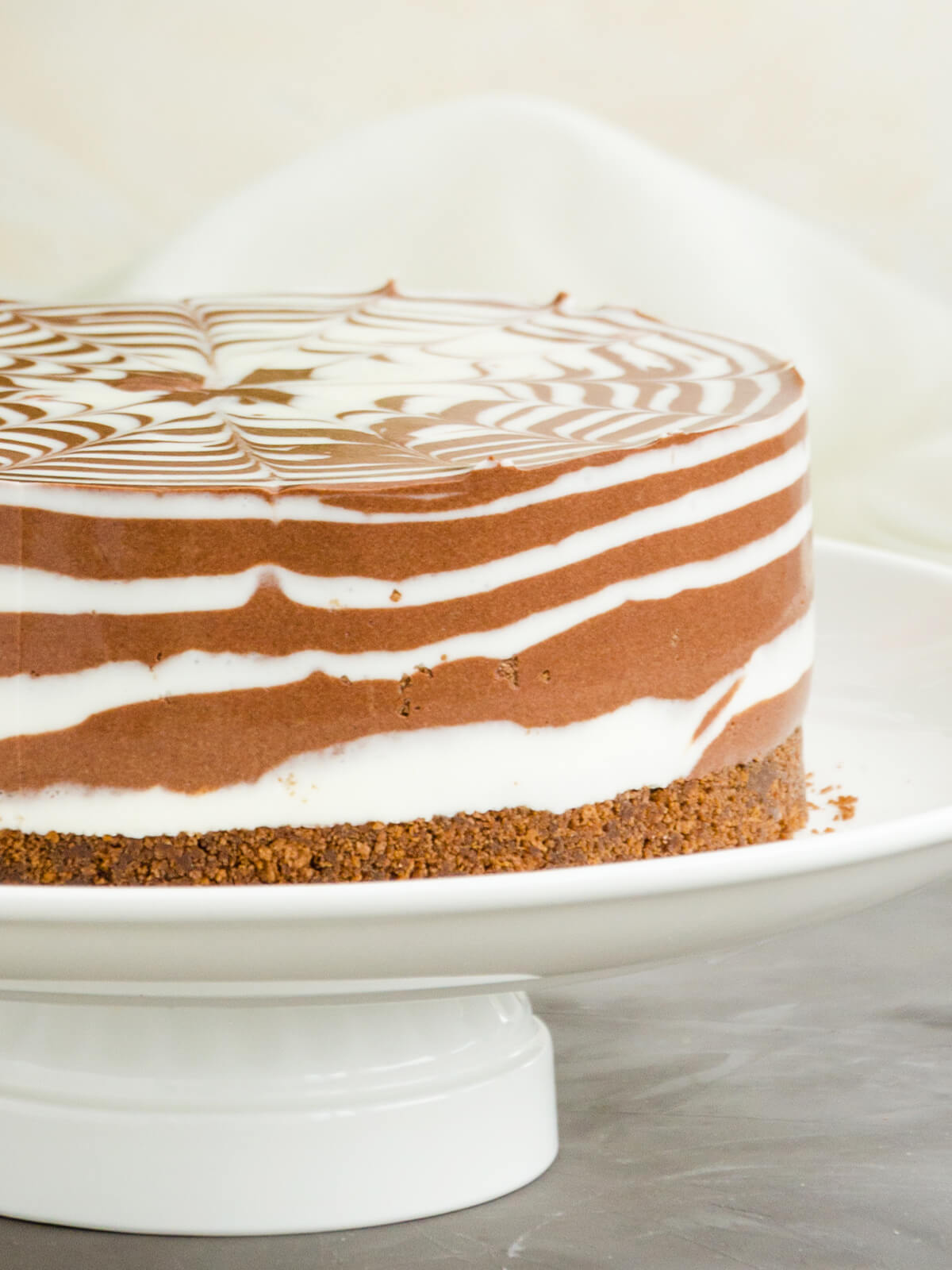 Zebra-Marmor-Cheesecake auf weißer Tortenplatte mit gewirbelter Oberfläche