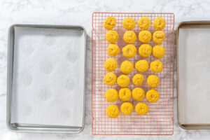 Frisch gebackene, sonnengelbe Zitronen-Cookies kühlen auf einem Kuchengitter zwischen zwei Backblechen aus