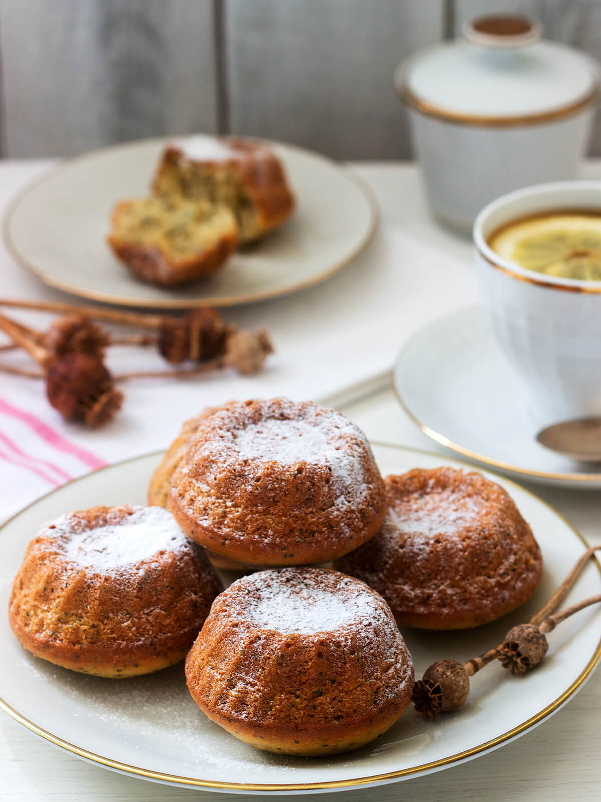 Mini-Gugelhupf-Muffins mit Zitrone und Mohn, mit Puderzucker bestäubt, neben Tasse Tee