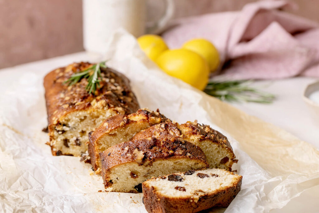 Zitronen-Pound-Cake mit Walnusskruste, Rosinen und Rosmarin, angeschnitten auf Backpapier