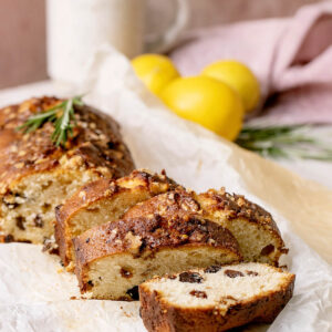 Zitronen-Pound-Cake mit Walnusskruste, Rosinen und Rosmarin, angeschnitten auf Backpapier