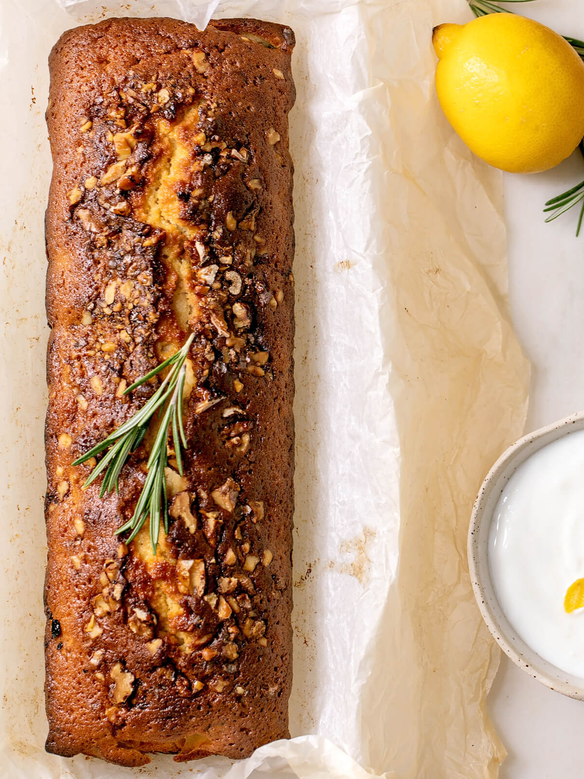 Zitronen-Pound-Cake mit knuspriger Walnusskruste und Rosmarin von oben, daneben Zitrone und Joghurt-Creme