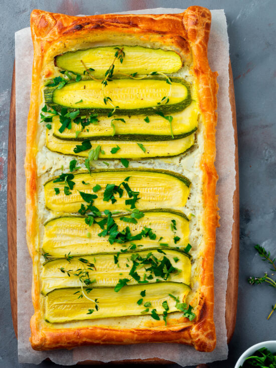 Rechteckige Zucchini-Ricotta-Tarte aus Blätterteig mit grünen und gelben Zucchini-Hälften längs auf Ricotta-Creme, mit Kräutern bestreut