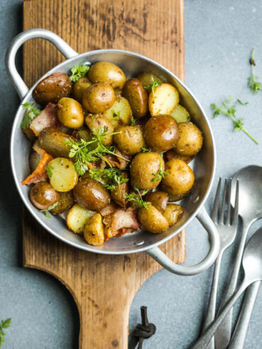 Junge Bratkartoffeln mit Speck und Petersilie in einer Pfanne, goldbraune kleine Kartoffeln mit Schale, knusprige Speckwürfel und frische Kräuter