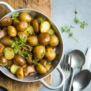 Junge Bratkartoffeln mit Speck und Petersilie in einer Pfanne von oben, goldbraune Kartoffeln mit Schale, knusprige Speckwürfel und frische Kräuter