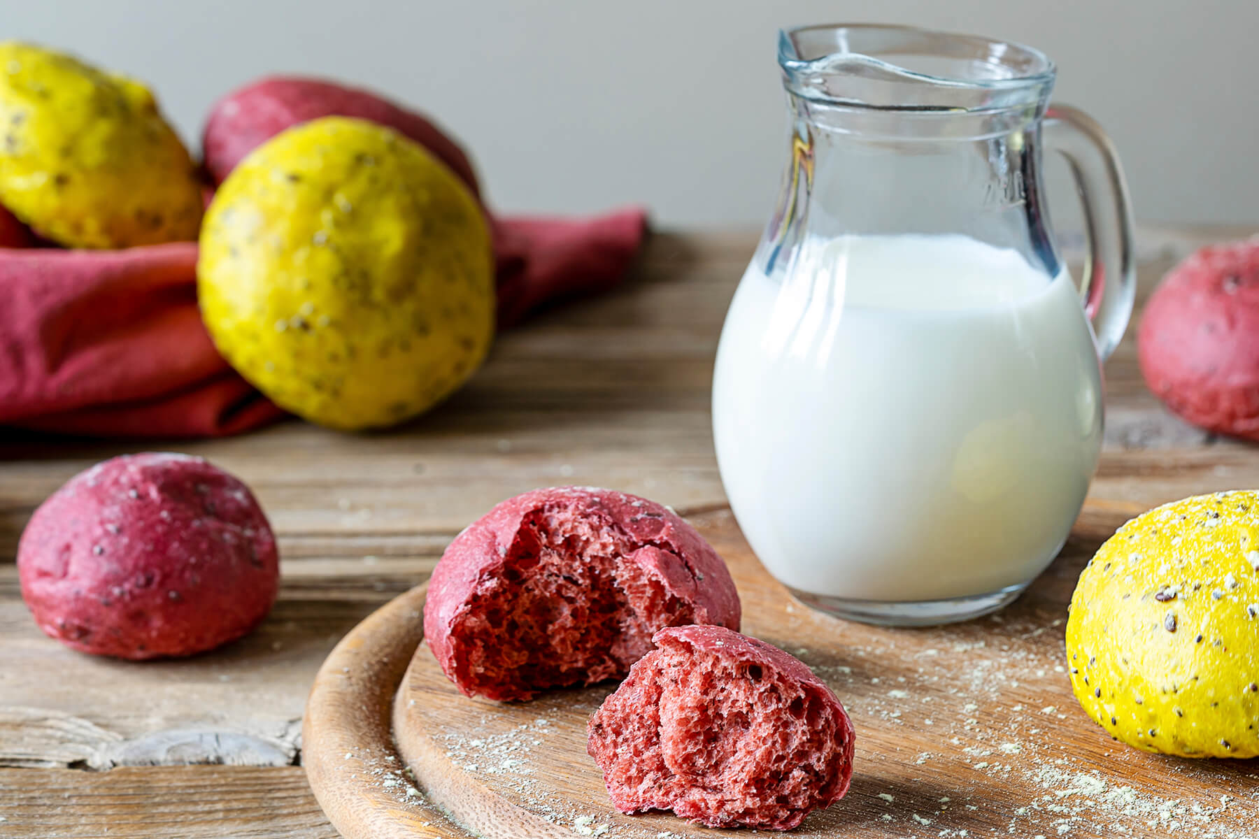 Ein aufgebrochenes pinkes Brötchen zeigt die weiche, rosa durchgefärbte Krume, daneben ein Krug mit Milch oder Pflanzendrink als Serviervorschlag