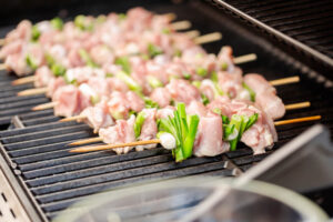Rohe Yakitori-Spieße mit Hähnchen-Oberschenkel und Frühlingszwiebel im Wechsel auf Bambusspießen, frisch auf den Grillrost gelegt
