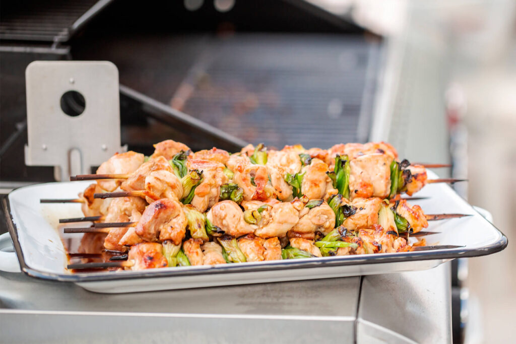 Fertig glasierte Yakitori-Spieße auf einem weißen Blech auf dem Grillwagen, hell bernsteinfarben glänzend