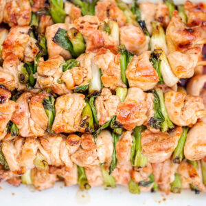 Glasierte Chicken-Yakitori-Spieße mit Frühlingszwiebel von oben auf weißem Blech, hell bernsteinfarben glänzend von der Yakitori-Tare