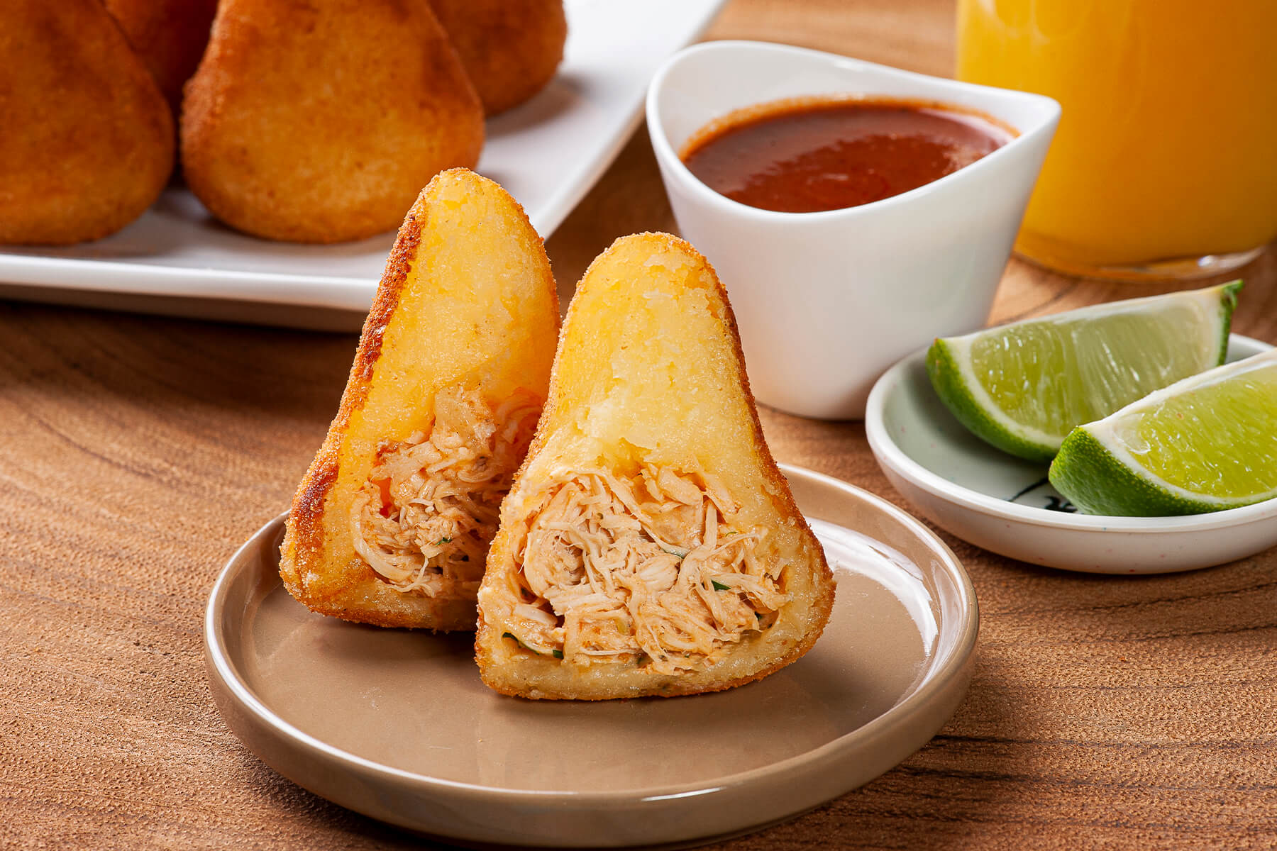 Aufgeschnittene Coxinha mit heller, saftiger Hähnchenfüllung aus zerzupfter Hähnchenbrust, daneben Limettenspalten und scharfer Dip