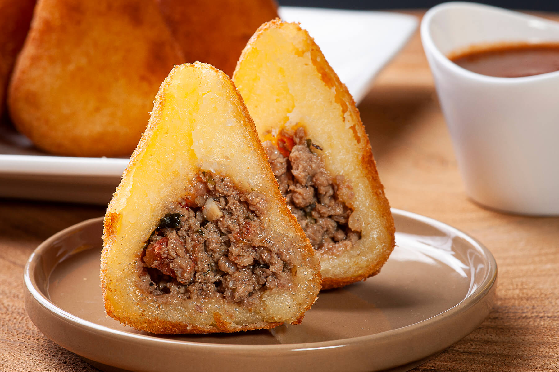 Aufgeschnittene Coxinha mit krümeliger, brauner Rinderhackfüllung mit roten Tomatenstückchen, auf einem hellen Teller