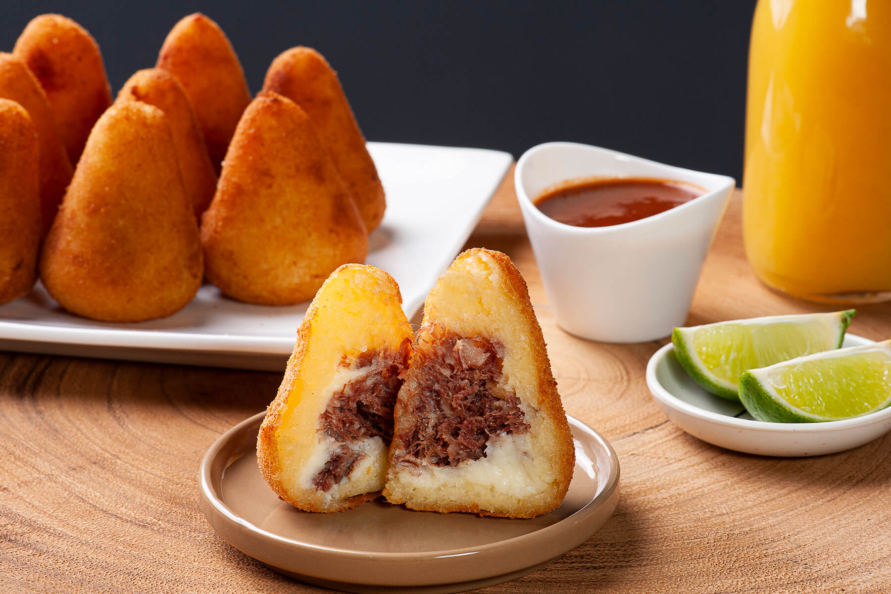 Aufgeschnittene Coxinha mit dunkler, faseriger Carne-Seca-Füllung und einer cremigen hellen Schicht aus Frischkäse, auf einem Teller