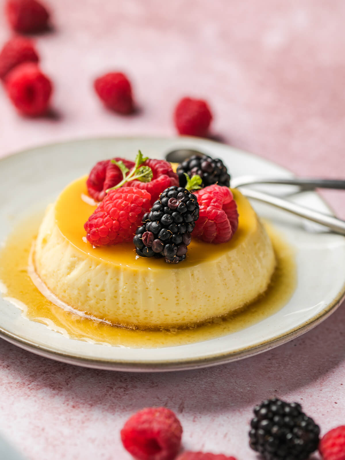 Gestürzte Crème Caramel mit Karamellschicht, frischen Himbeeren, Brombeeren und Minze auf einem hellen Teller