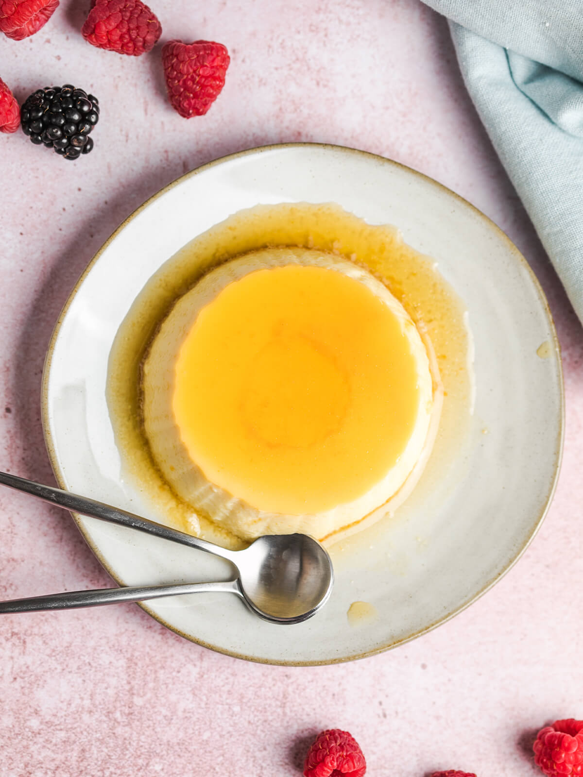 Gestürzte Crème Caramel von oben fotografiert, mit flüssiger Karamellschicht und zwei Löffeln auf einem rustikalen Teller