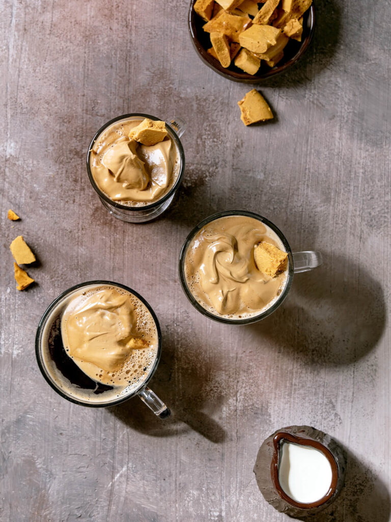 Drei Gläser Dalgona-Kaffee von oben mit dick aufgeschlagener Kaffeecreme und knusprigen Dalgona-Bonbon-Splittern