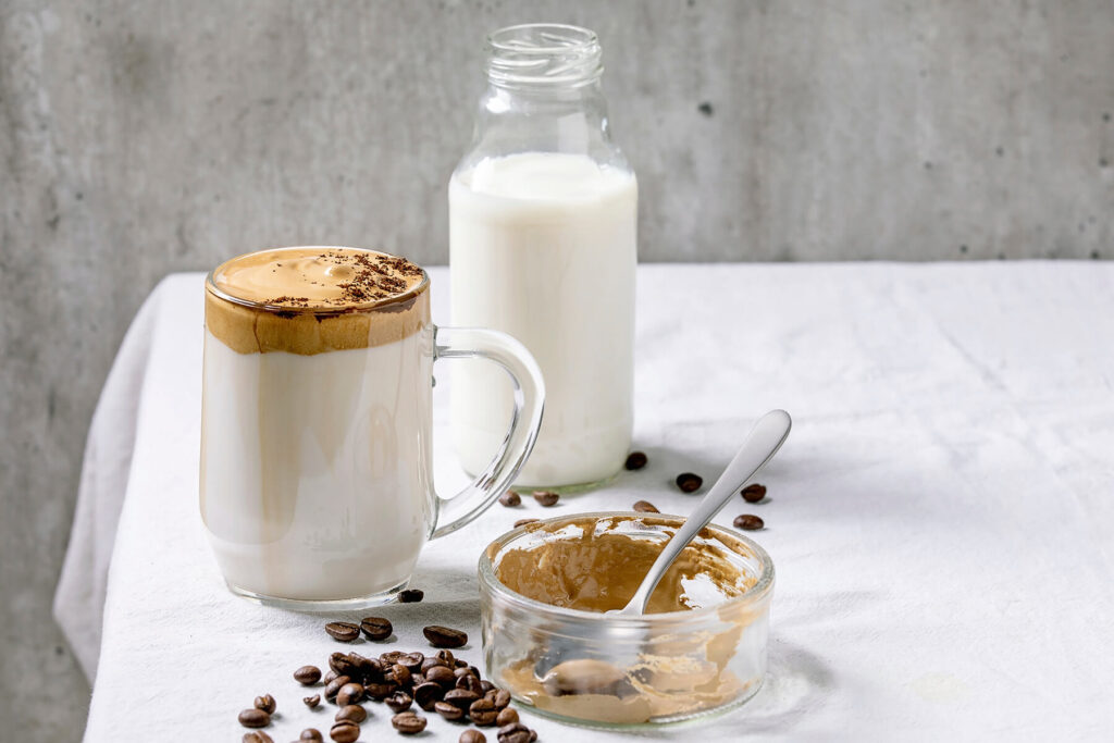 Fertiger Dalgona-Kaffee im Glasbecher daneben eine kleine Milchflasche, bereit zum Servieren