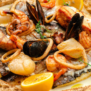 Nahaufnahme einer Fisch- und Meeresfrüchte-Pfanne in heller Sahnesauce mit gegrilltem Lachs, weißem Fisch, Garnelen, Calamari, Miesmuscheln, Oktopus und Jakobsmuscheln