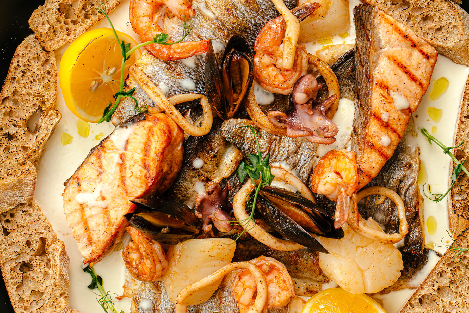 Fisch- und Meeresfrüchte-Pfanne von oben mit gegrilltem Lachs, weißem Fisch, Miesmuscheln, Oktopus, Garnelen und Jakobsmuscheln in heller Sahnesauce