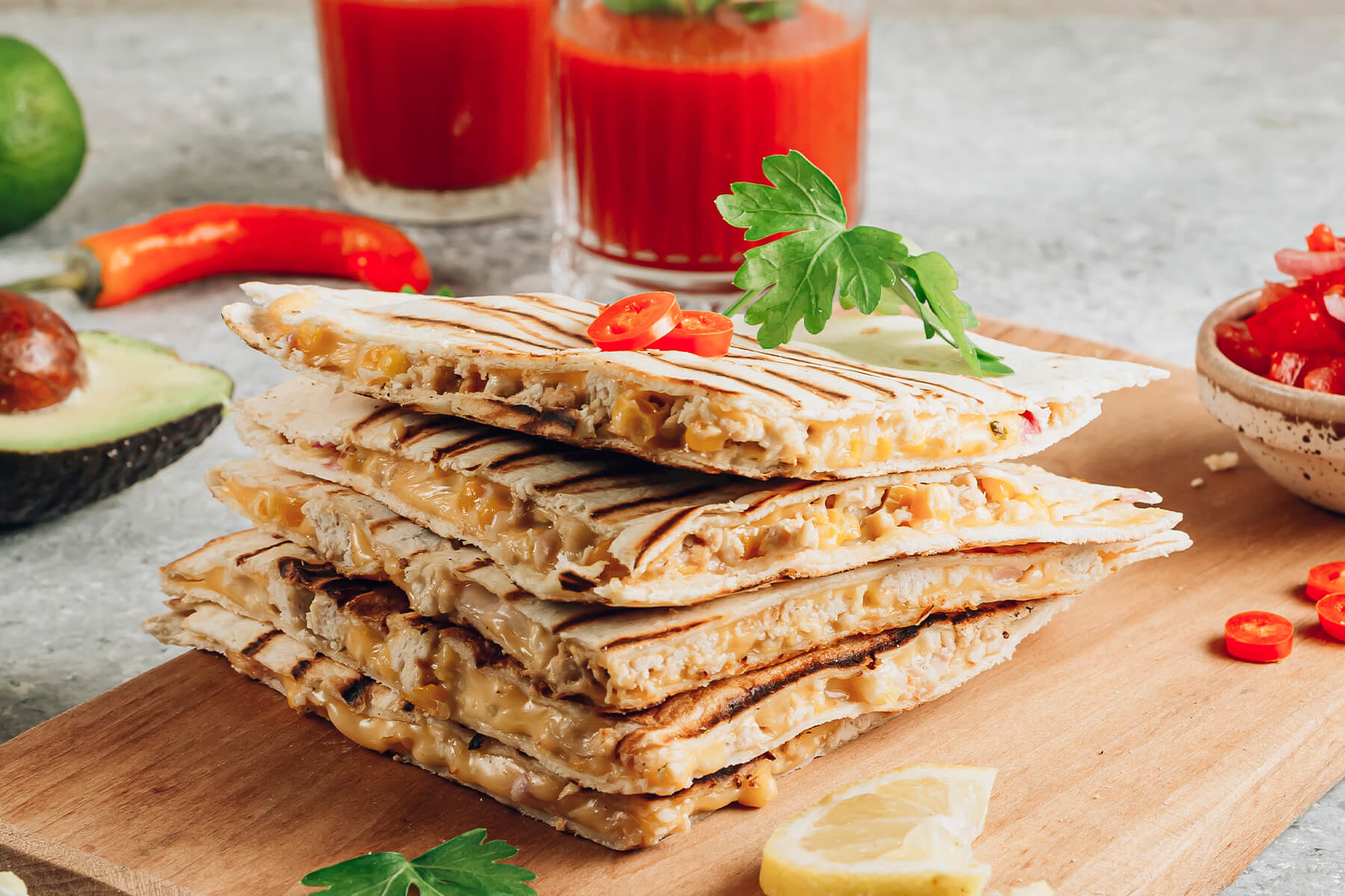 Gestapelte gegrillte Quesadilla-Ecken mit geschmolzenem Käse, Mais und Hähnchen in der Füllung, daneben Avocado, Chili und Tomaten-Salsa