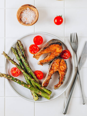 Gegrillter Lachs mit grünem Spargel, Kirschtomaten und grobem Salz auf hellem Teller, mediterran angerichtet von oben