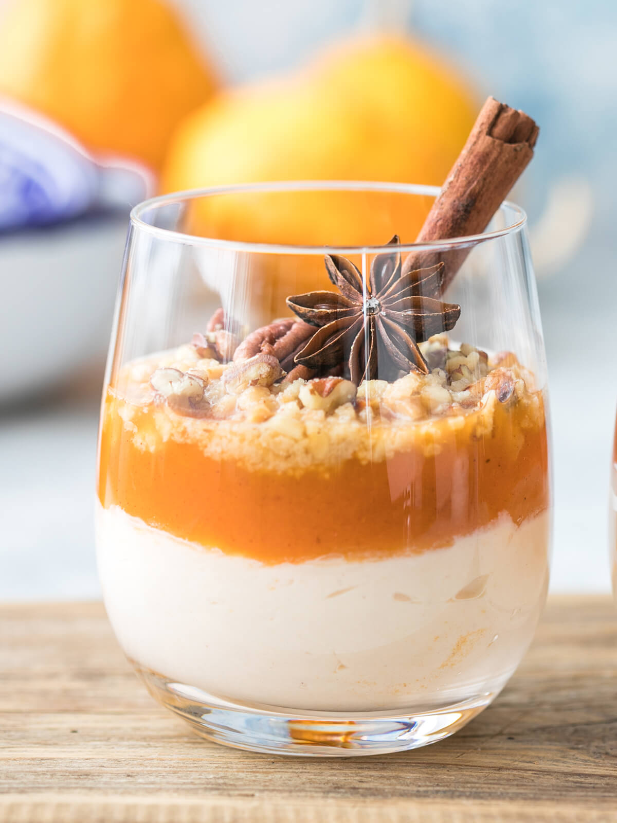 Herbstliches Kürbis-Trifle im Glas mit heller Frischkäse-Creme, glänzender oranger Kürbisschicht und gehackten Pekannüssen, garniert mit Zimtstange und Sternanis