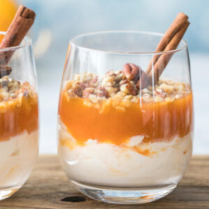 Zwei Gläser herbstliches Kürbis-Trifle mit heller Frischkäse-Creme, glänzender oranger Kürbisschicht und gehackten Pekannüssen, garniert mit Zimtstange und Sternanis