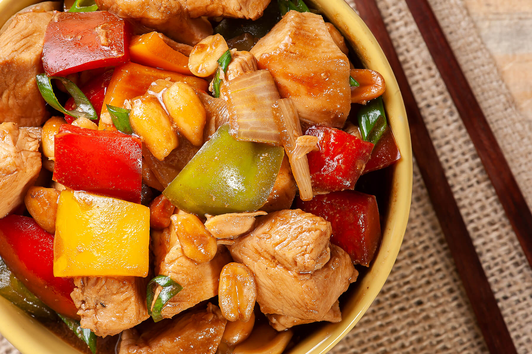 Nahaufnahme von Kung Pao Chicken mit goldbraunen Hähnchenwürfeln, roter, grüner und gelber Paprika, Erdnüssen und Frühlingszwiebeln in glänzender Sauce