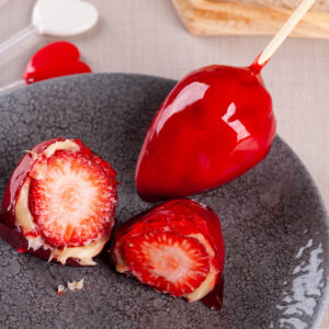 Morango do Amor aufgeschnitten – ganze Erdbeere, weiße Cremeschicht und glänzend rote Zuckerhülle auf grauem Teller