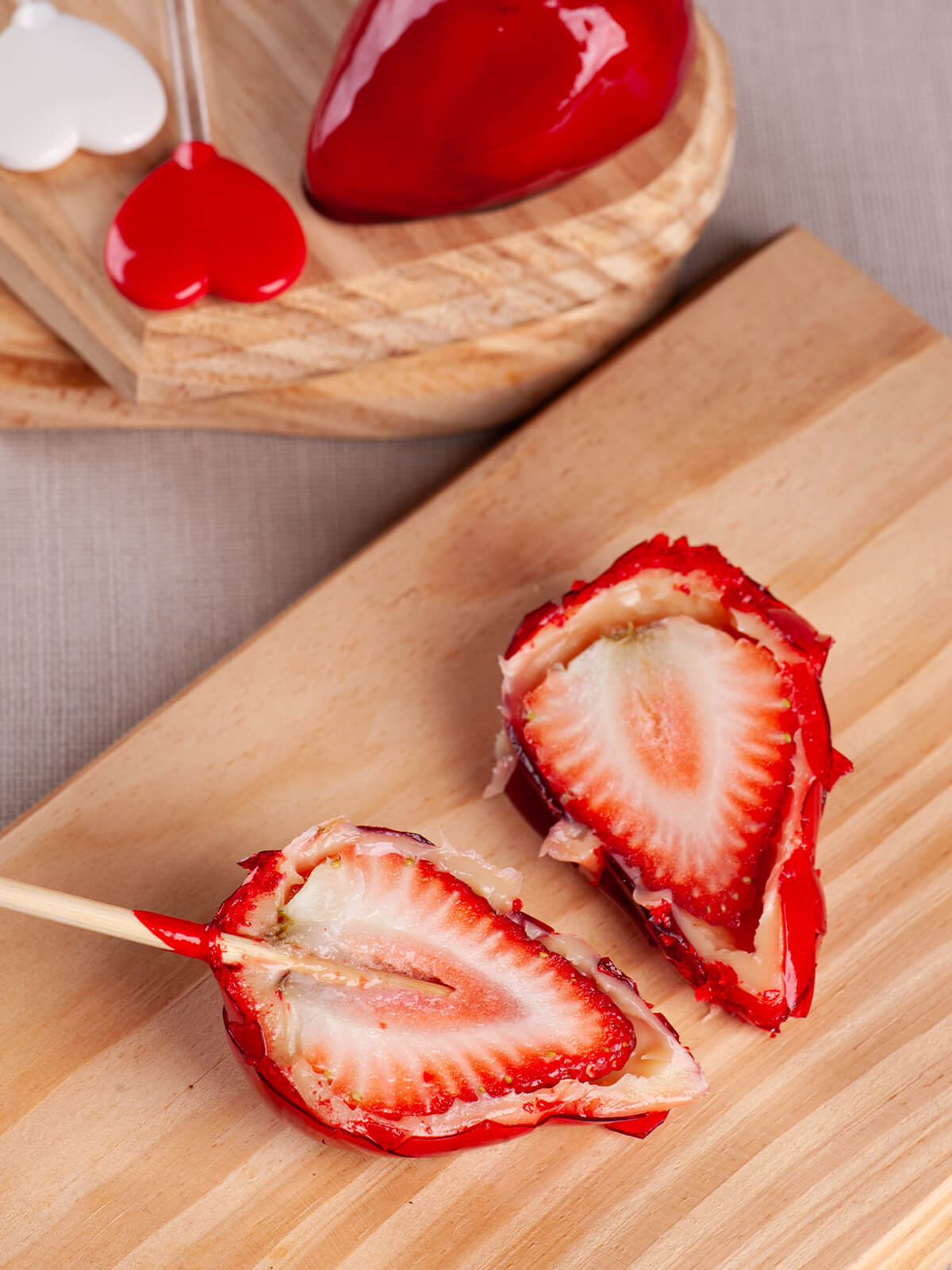 Zwei Hälften einer Morango do Amor auf Holzbrett, Schnittfläche zeigt Erdbeere, weiße Creme und rote Hülle