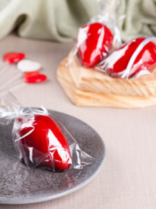 Drei fertige Morango do Amor einzeln in klare Tüten gewickelt als Gastgeschenk auf Teller und Holzbrett