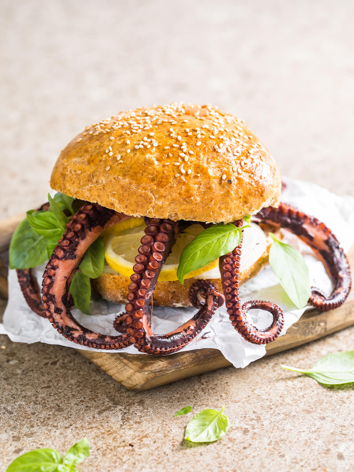 Oktopus-Burger im goldenen Sesambrötchen mit dramatisch heraushängenden Tentakeln, Zitronenscheibe und frischem Basilikum auf einem Holzbrett