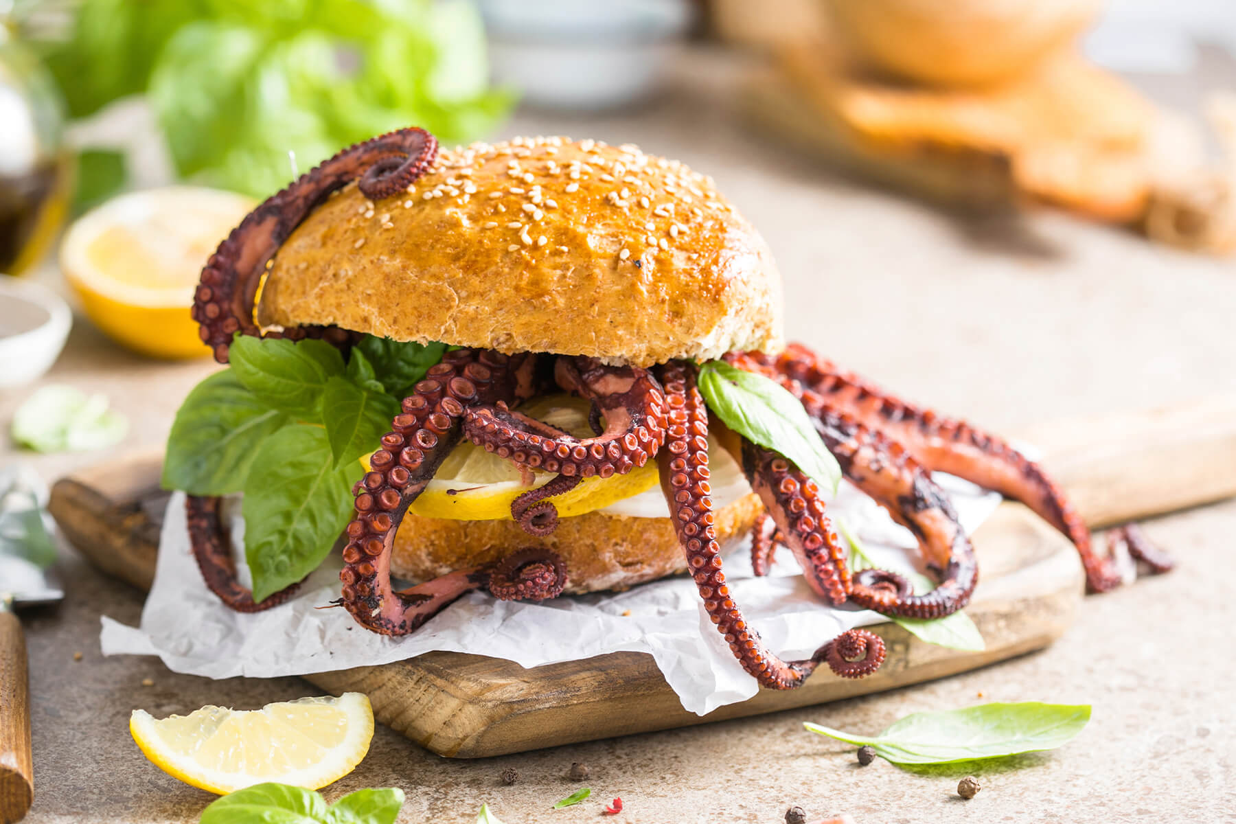 Oktopus-Burger von der Seite mit heraushängenden Tentakeln, Zitronenscheibe, Basilikum und heller Sauce auf weißem Papier