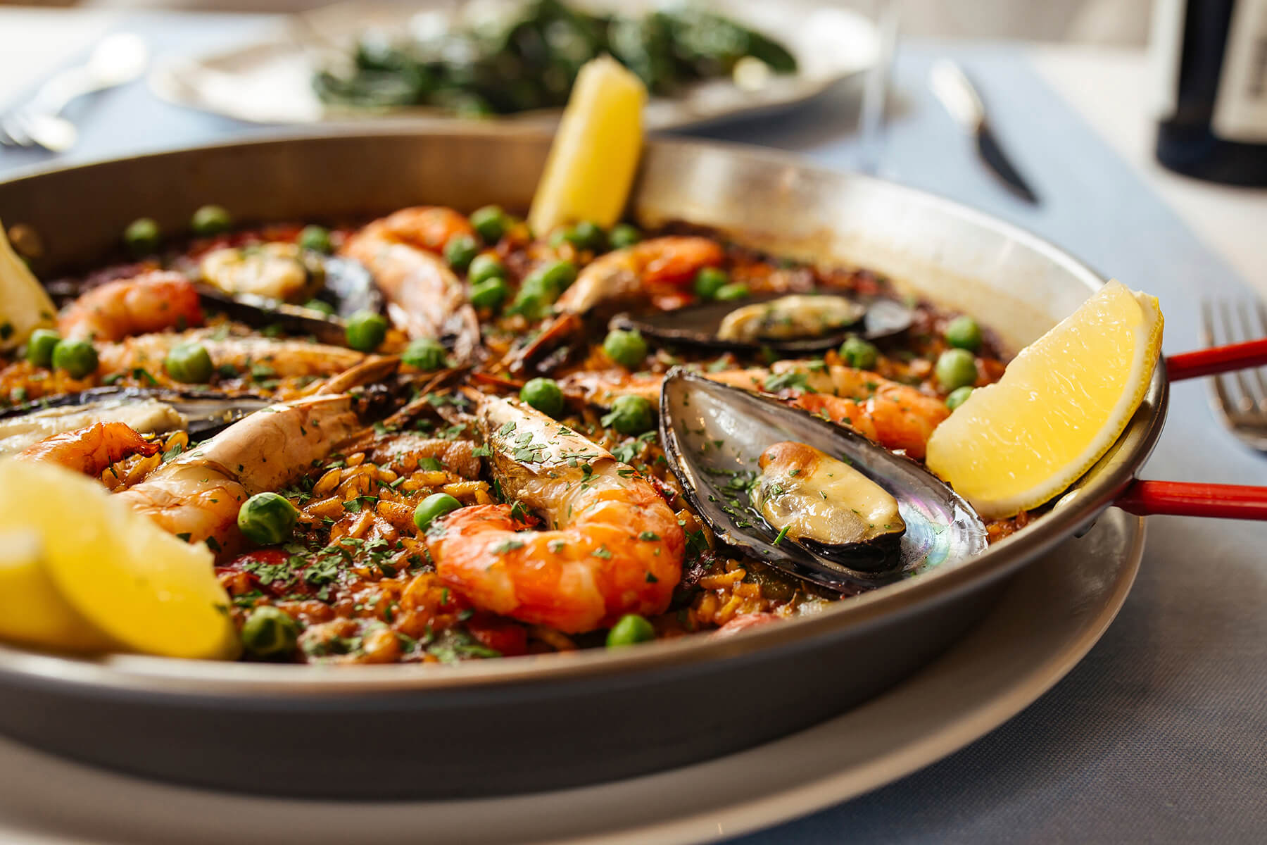 Nahaufnahme der spanischen Paella de Marisco mit glänzenden Garnelen, geöffneten Miesmuscheln, grünen Erbsen und Petersilie auf safranrotem Reis