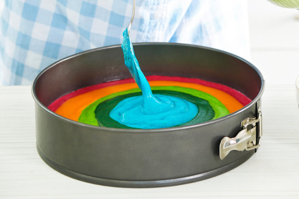 Blaue Lebensmittelfarbe wird mittig in die bereits entstandenen Farbringe gegossen