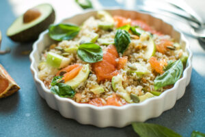 Reissalat mit Grapefruit von der Seite in einer flachen weißen geriffelten Form, mit rosa Grapefruit-Filets, grünen Apfelspalten, Avocadoscheiben, gerösteten Kürbiskernen und Basilikumblättern